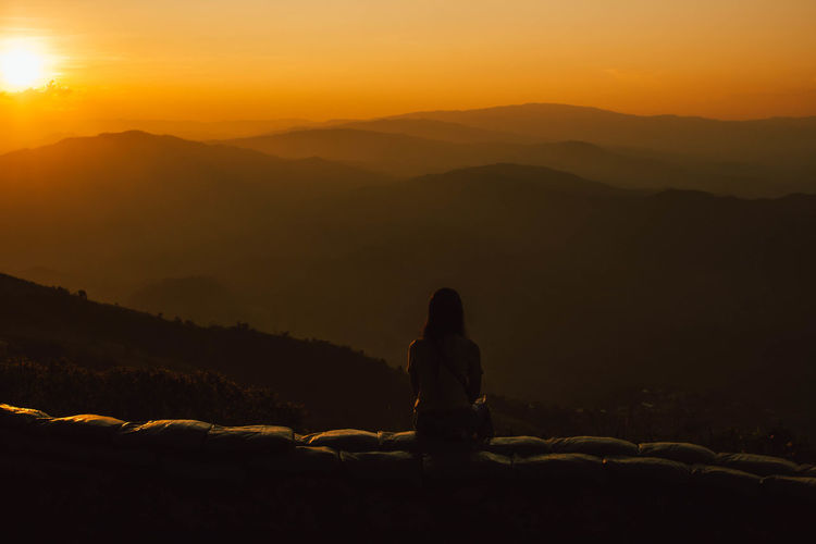 Silhouette women looking at mountains against sky during sunset