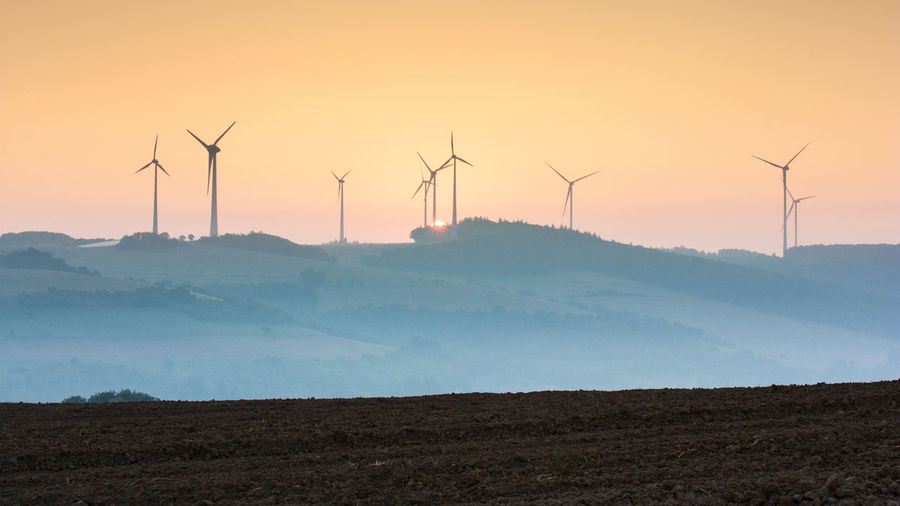 Wind turbines on field against sky during sunset