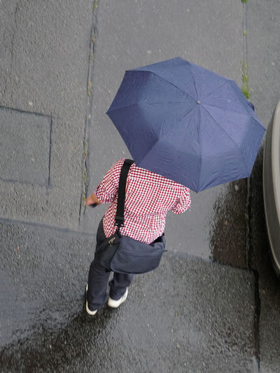 High angle view of man holding umbrella while walking on road during rainy season