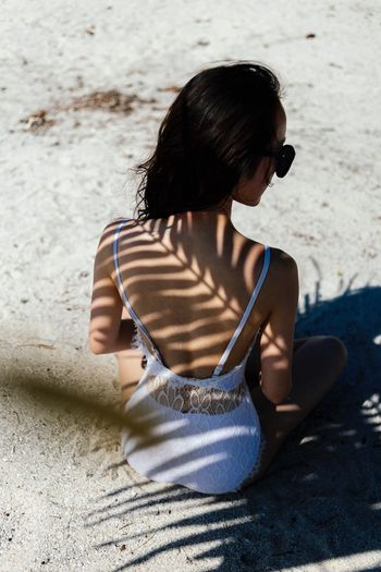 Rear view of woman sitting at beach during sunny day