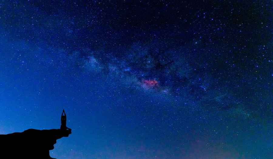 Silhouette person performing exercise on mountain against star field at night