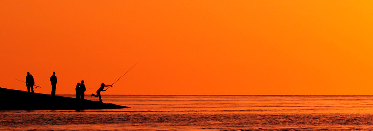 Silhouette people fishing on shore at beach against sky during sunset