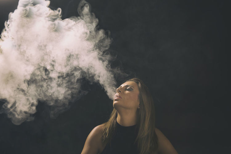 Woman exhaling smoke against wall
