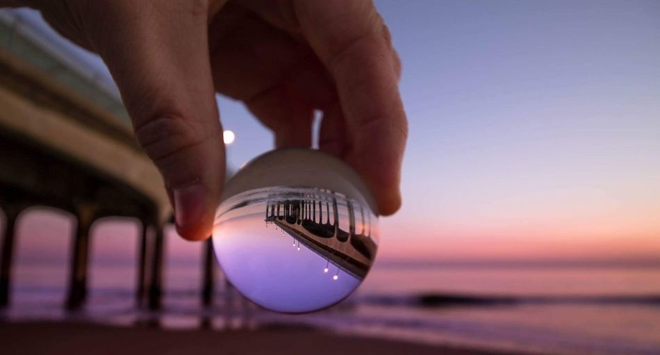 Person holding crystal lens with reflection of bridge