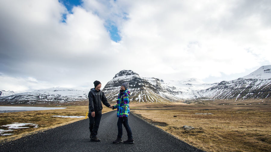 Full length of couple standing on road against cloudy sky