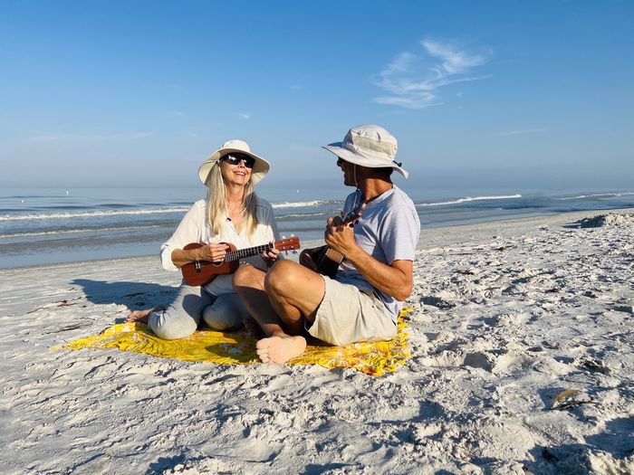 Senior couple having fun together playing ukeleles sitting on beach in florida in early morning sun