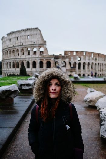 Young woman in fur coat standing against coliseum