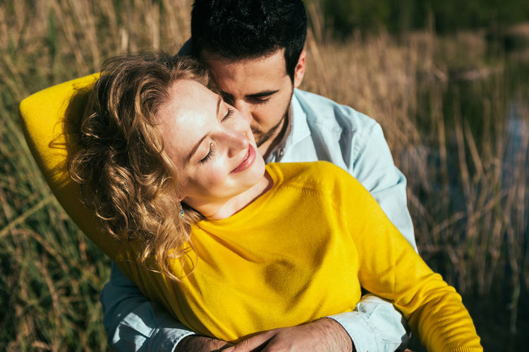 Delighted girlfriend and calm boyfriend hugging while standing together in field on sunny day