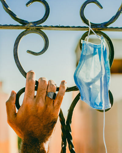 Close-up of hand holding grill and hanging mask against blue sky