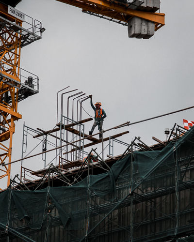 Low angle view of worker working at construction site against clear sky