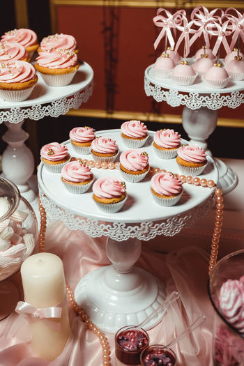 Cupcakes with pink cream and decorated with golden pastry beads on a white tray