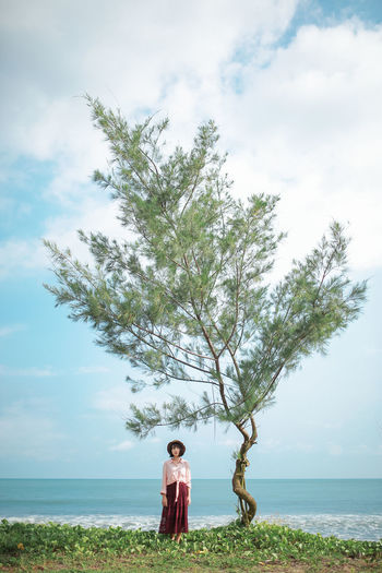Woman standing by tree at beach against sky