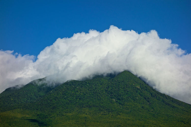 Low angle view of green mountain against cloudy blue sky