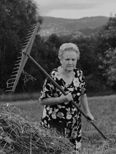 Senior woman with rake walking on grassy field