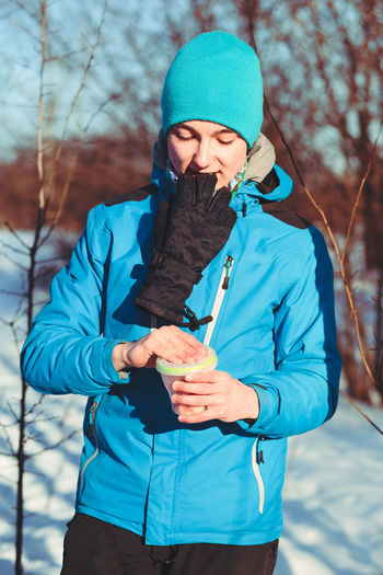 Young female hiker opening food container on snowy field