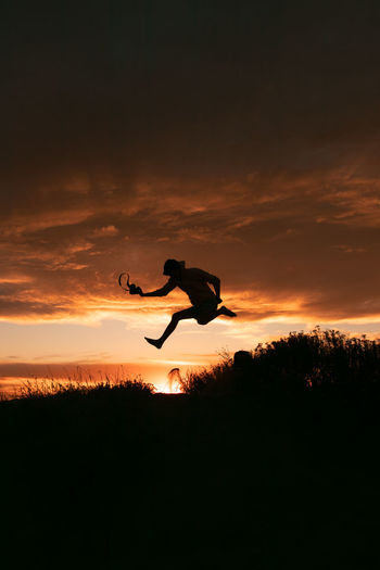 Silhouette man jumping against orange sky