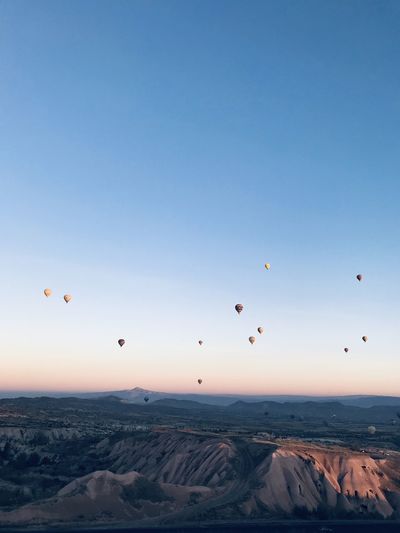 Hot air balloons flying over landscape against sky during sunset