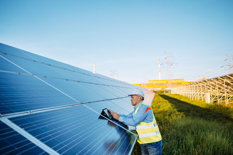 Mature industrial worker using tablet while monitoring rows of photovoltaic solar panels