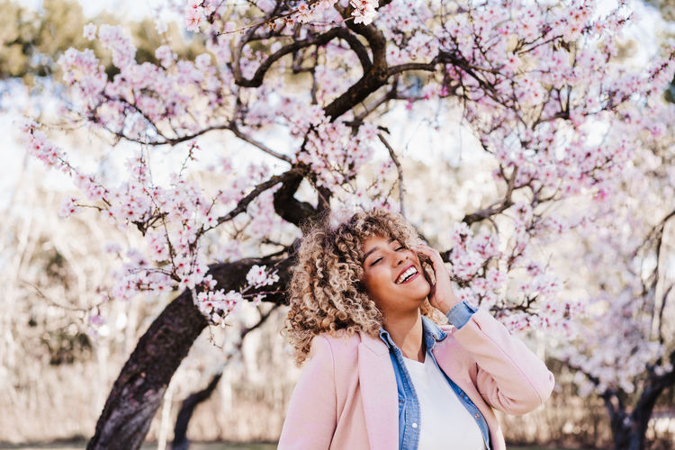 Portrait of beautiful hispanic woman with afro hair in spring among pink blossom flowers. nature