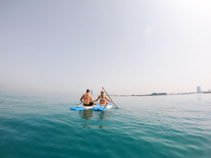 People on paddle board in sea against sky