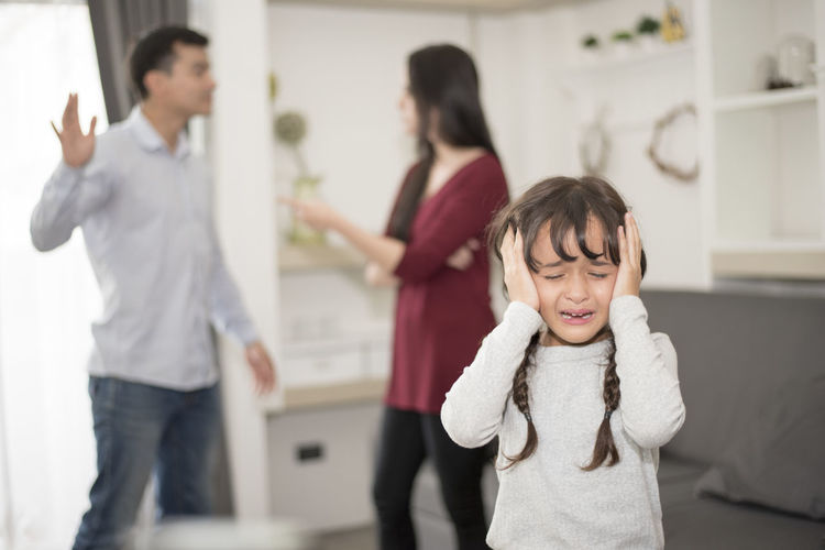 Close-up of girl crying while parents fighting in background at home