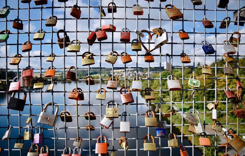 Full frame shot of padlocks hanging on fence against sky