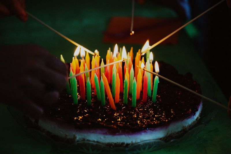 Close-up of hands burning incenses from multi colored candles on cake