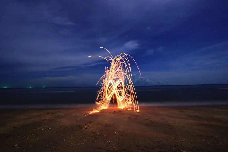 Light trails on beach against sky at night