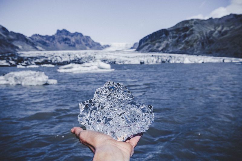Person holding ice on sea against mountain