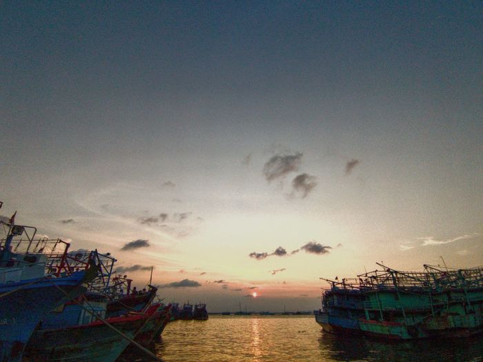 Fishing boats moored at harbor against sky during sunset