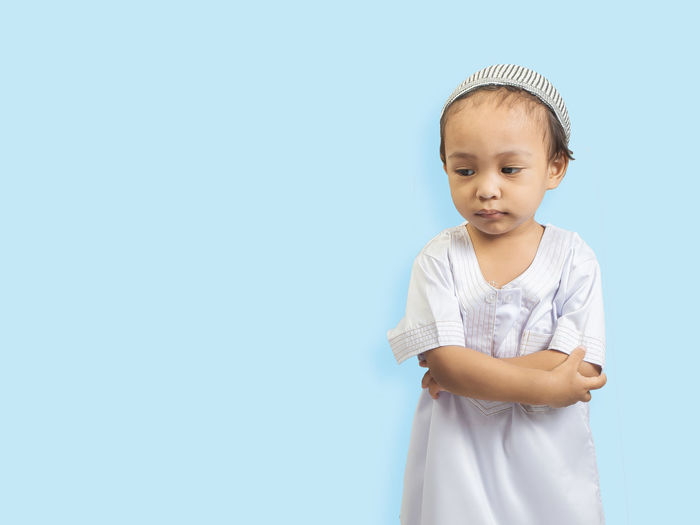 Cute boy wearing traditional clothing standing against blue background