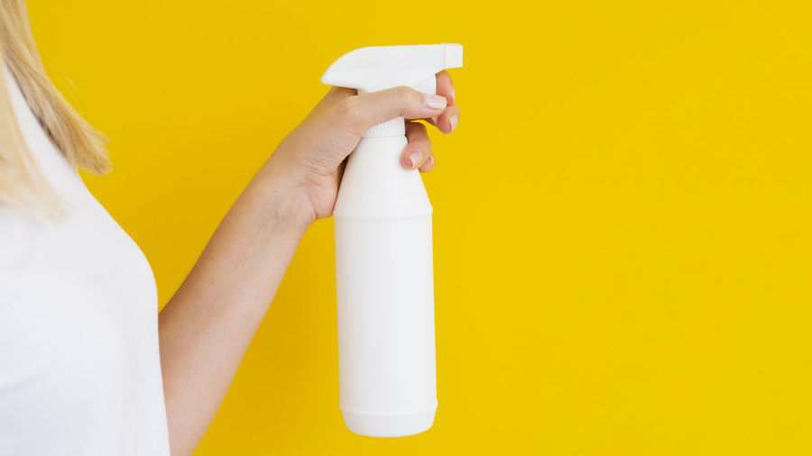 Midsection of woman holding bottle against yellow background