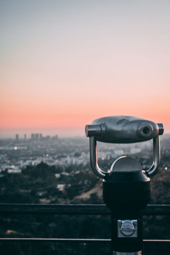 Close-up of coin-operated binoculars against cityscape during sunset