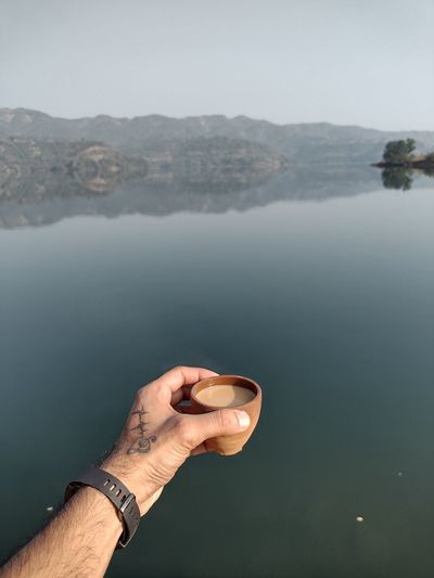 Midsection of person holding rock by lake against sky