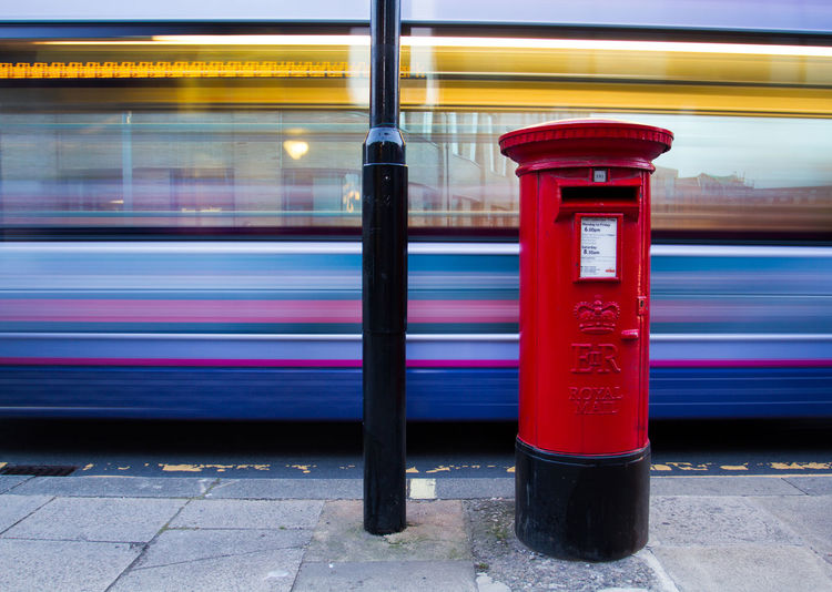 Red public mailbox against blurred motion of bus