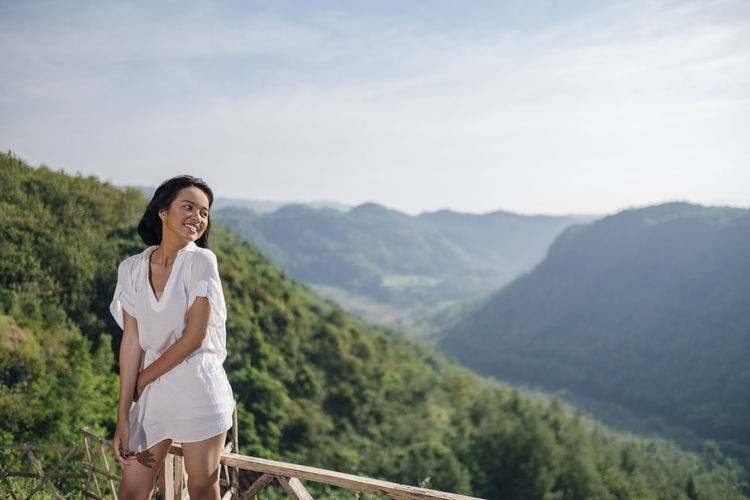 Smiling woman standing by railing against mountains and sky