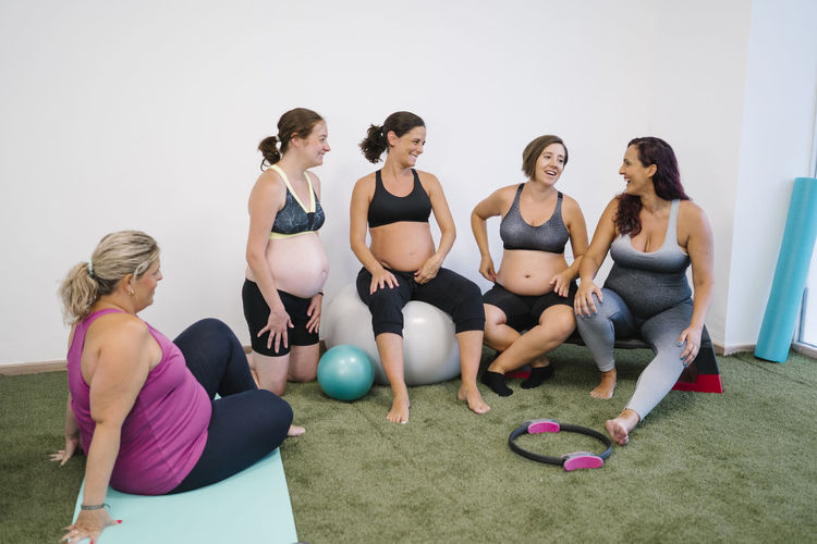 Group of pregnant females laughing while doing exercise at yoga studio