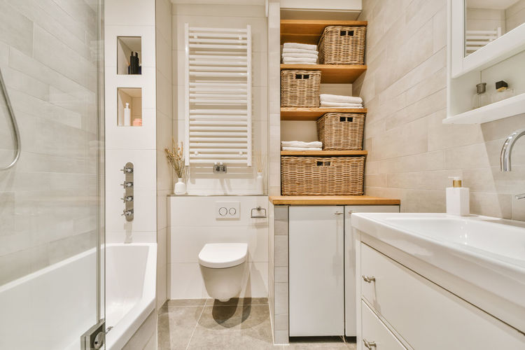 Modern bathroom with bathtub and wooden shelves near ceramic sink under mirror