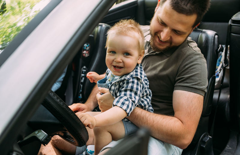 Dad shows his little son how to drive car while sitting behind wheel