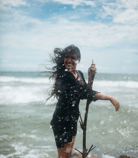Portrait of smiling young woman standing in sea against sky