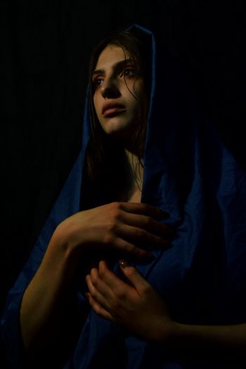 Thoughtful woman with hand on breast standing against black background