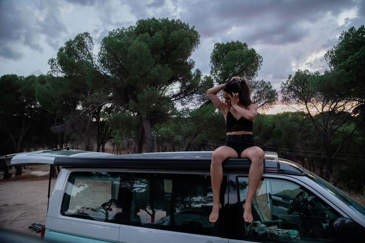 Full length of woman sitting on car against trees