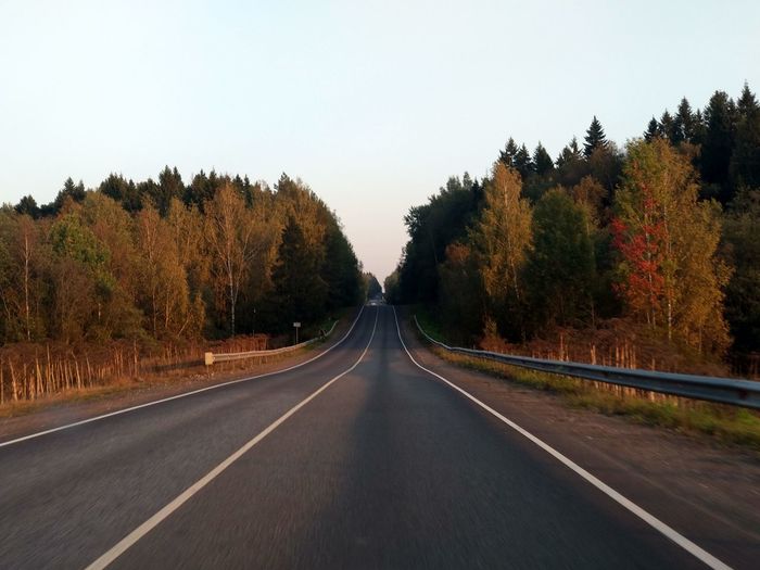 Empty road along trees and against clear sky