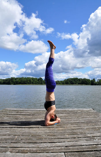 Full length of young woman doing headstand on jetty by lake