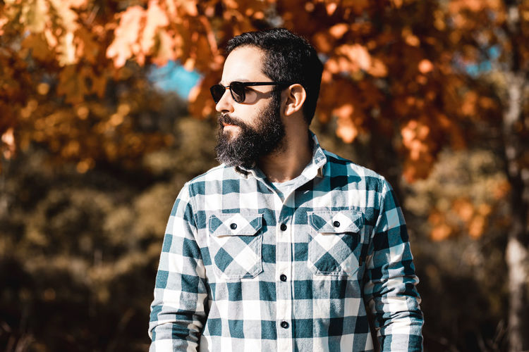 Man wearing sunglasses looking away while standing against trees