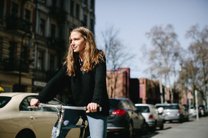 Smiling young woman with bicycle on street in city