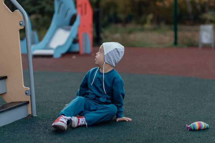 A boy, person with down syndrome sits on rubber ground in the park