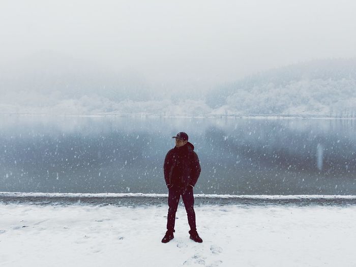 Full length of man standing against lake during snowfall