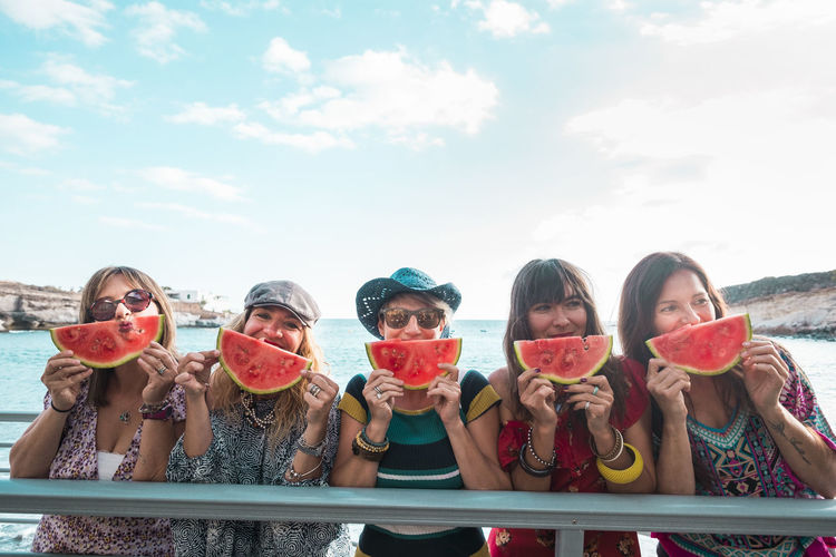 Friends holding watermelon slices against sea and sky