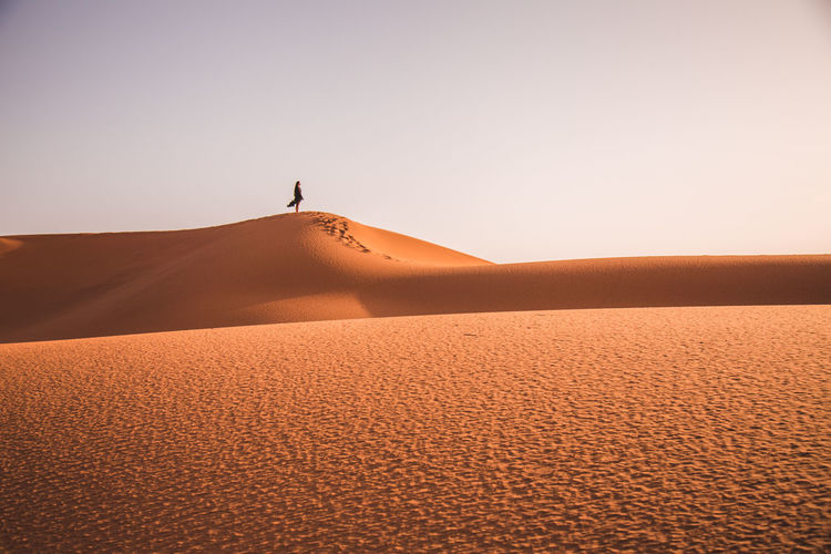 Full length of woman standing on sand dune in desert against sky